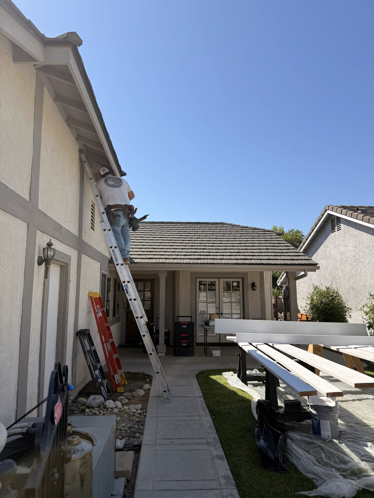 A custom home under a clear Santa Clarita sky with a crew member on a ladder.